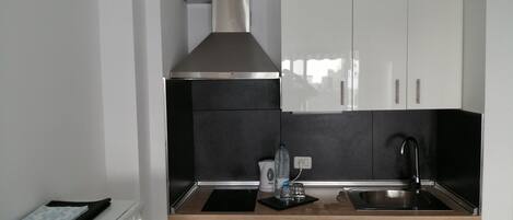 Une cuisine compacte avec des meubles blancs, une hotte en acier inoxydable, un évier et un lave-vaisselle.
