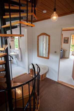 A spiral staircase with wooden steps and black railings, leading to a room with a white sink, mirror, and fluffy white chair.