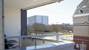 A balcony with a table and chairs, overlooking a park and a building with a clock. - Marianne in the Ankerlicht house (Westerland)