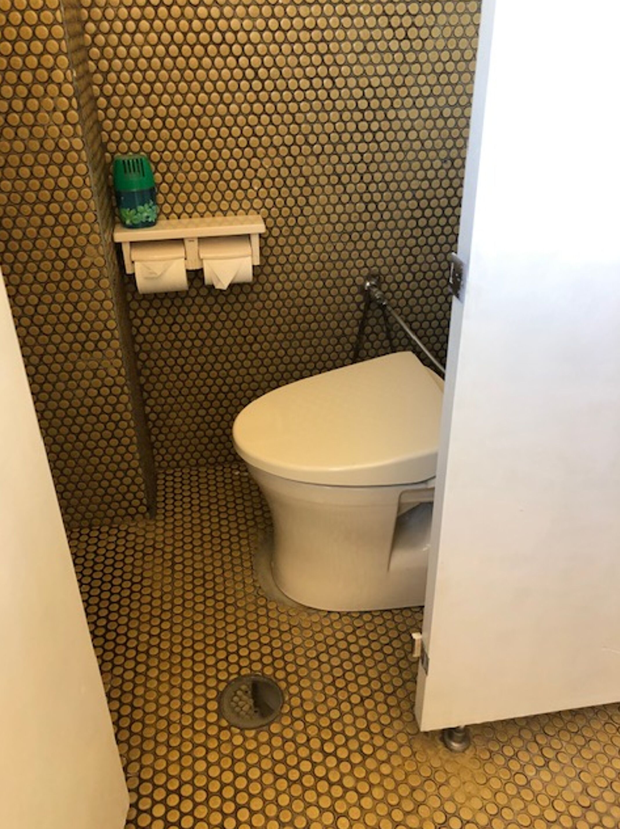 Un baño con inodoro, lavamanos y una botella verde en un estante.