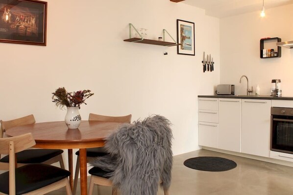 A modern kitchen with white cabinets, a built-in oven, and a dining area with a wooden table and chairs.