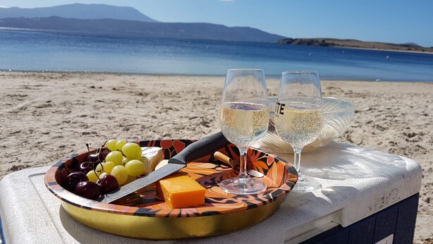 Une table installée sur la plage, avec un plateau de fruits, du fromage et des verres de vin blanc.