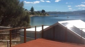 Une terrasse en bois avec une rambarde donnant sur un lac, entourée d’arbres et de collines.
