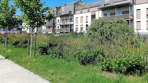 Ein modernes Mehrfamilienhaus mit mehreren Balkonen, einem Kiesweg und umgebendem Grün.