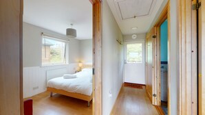 A bedroom with a bed, a window, and a door leading to another room. - E46 Dunroven, Riviere Towans (Hayle)