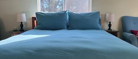 A bedroom with a large bed, two bedside tables with lamps, a window with blinds, and a chair.