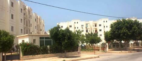 A multi-story residential building with a flat facade, a gated entrance, and a clear sky.