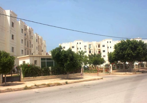 A multi-story residential building with a flat facade, a gated entrance, and a clear sky.