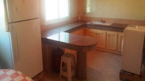 Cuina compacta amb nevera, un rentapeus i una petita zona de dinar amb un tamboret.