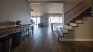 Amplia sala de estar con escalera de madera, una mesa de comedor y un gran ventanal que proporciona luz natural.