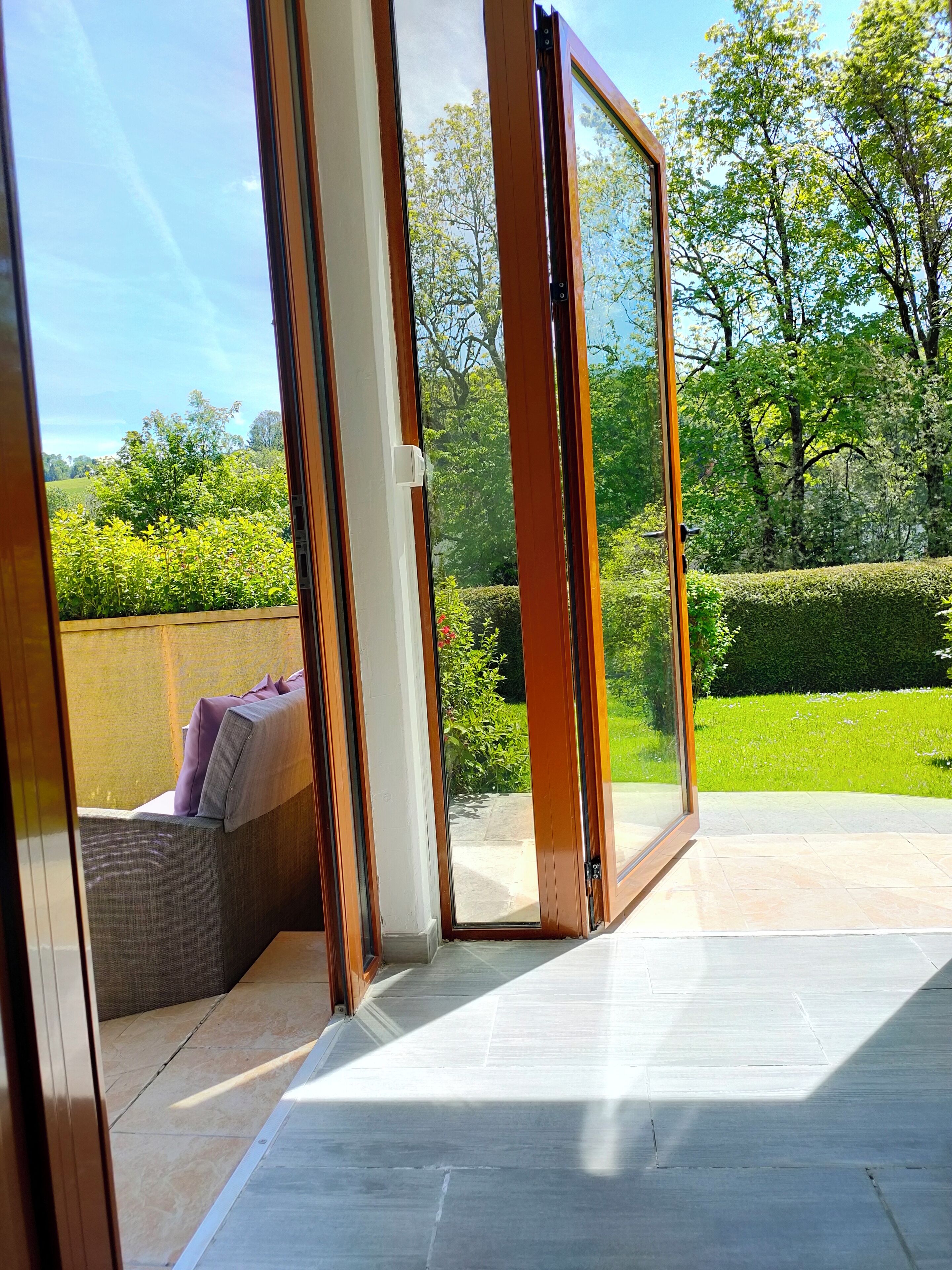 Une terrasse moderne avec une porte-fenêtre coulissante donnant sur un jardin luxuriant.
