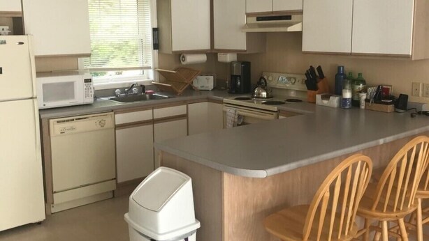 A kitchen with white cabinets, a stainless steel island with bar stools, a dishwasher, a microwave, and a sink. - Spacious Condo on Sunday River Access Road (Bethal)