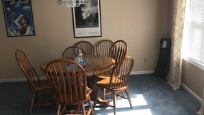 A dining area with a round table and six wooden chairs, a ceiling light, and two framed pictures on the wall. - Spacious Condo on Sunday River Access Road (Bethal)