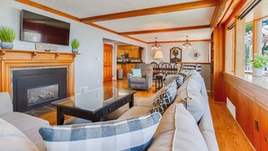 A living room with a fireplace, a television, and a dining area with wooden cabinets. - Long View on the Cove: Views! Views! Views! (Seneca Falls)