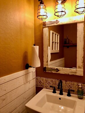 A bathroom with a white sink, two black faucets, a mirror with a white frame, and a towel hanging on the wall. - COZY condo located on Mill St. in downtown historic Grass Valley. (Grass Valley)
