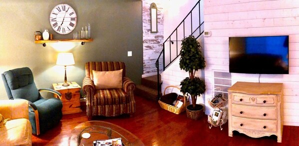 A living room with a sofa, armchair, TV, wooden cabinet, and a staircase. - COZY condo located on Mill St. in downtown historic Grass Valley. (Grass Valley)