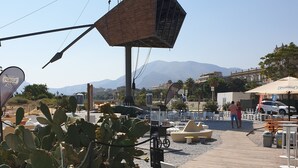 A wooden deck with outdoor seating, a cactus plant, and a view of mountains in the background.