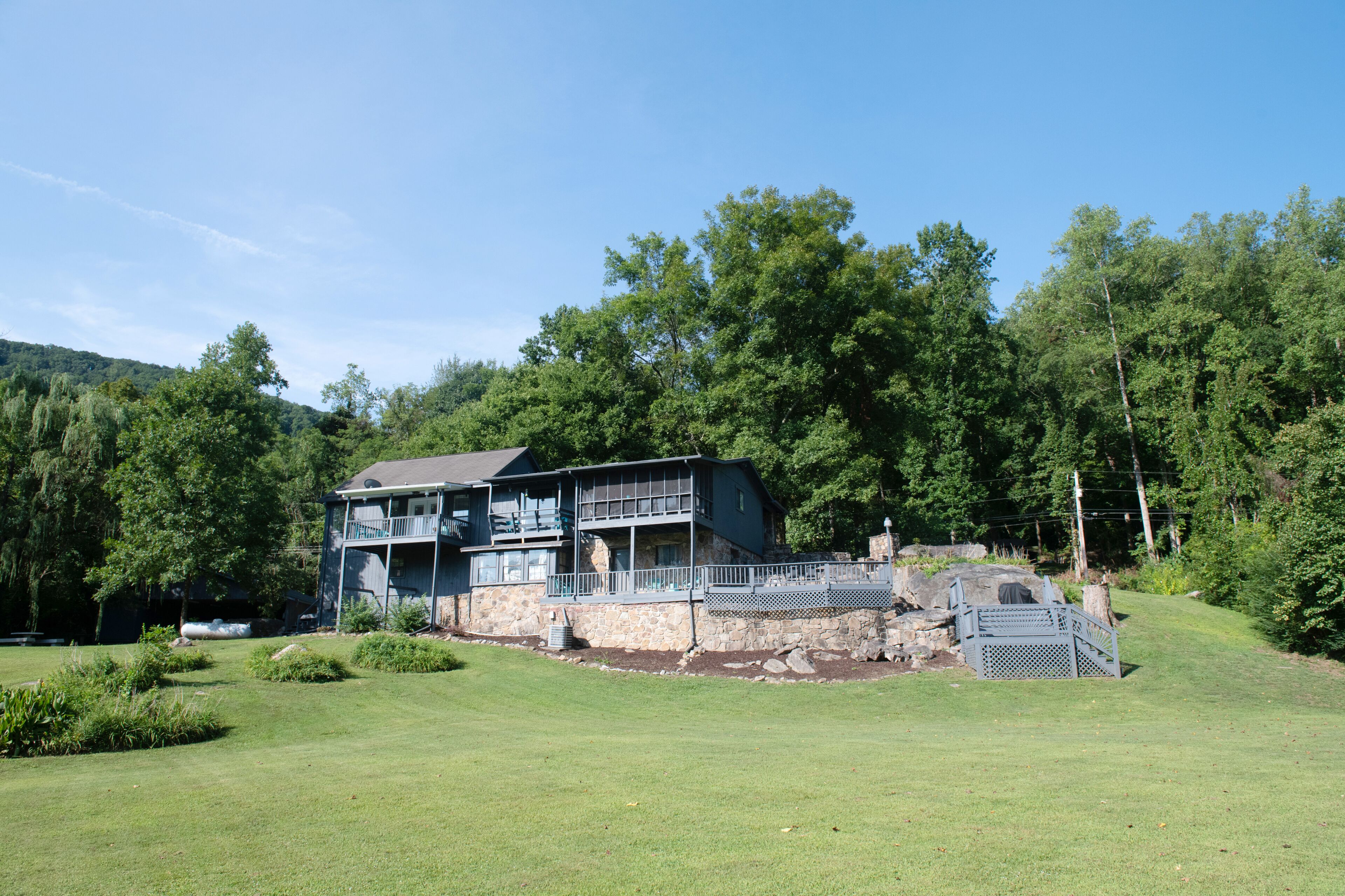 A two-story building with a balcony, surrounded by a well-maintained lawn and dense trees.