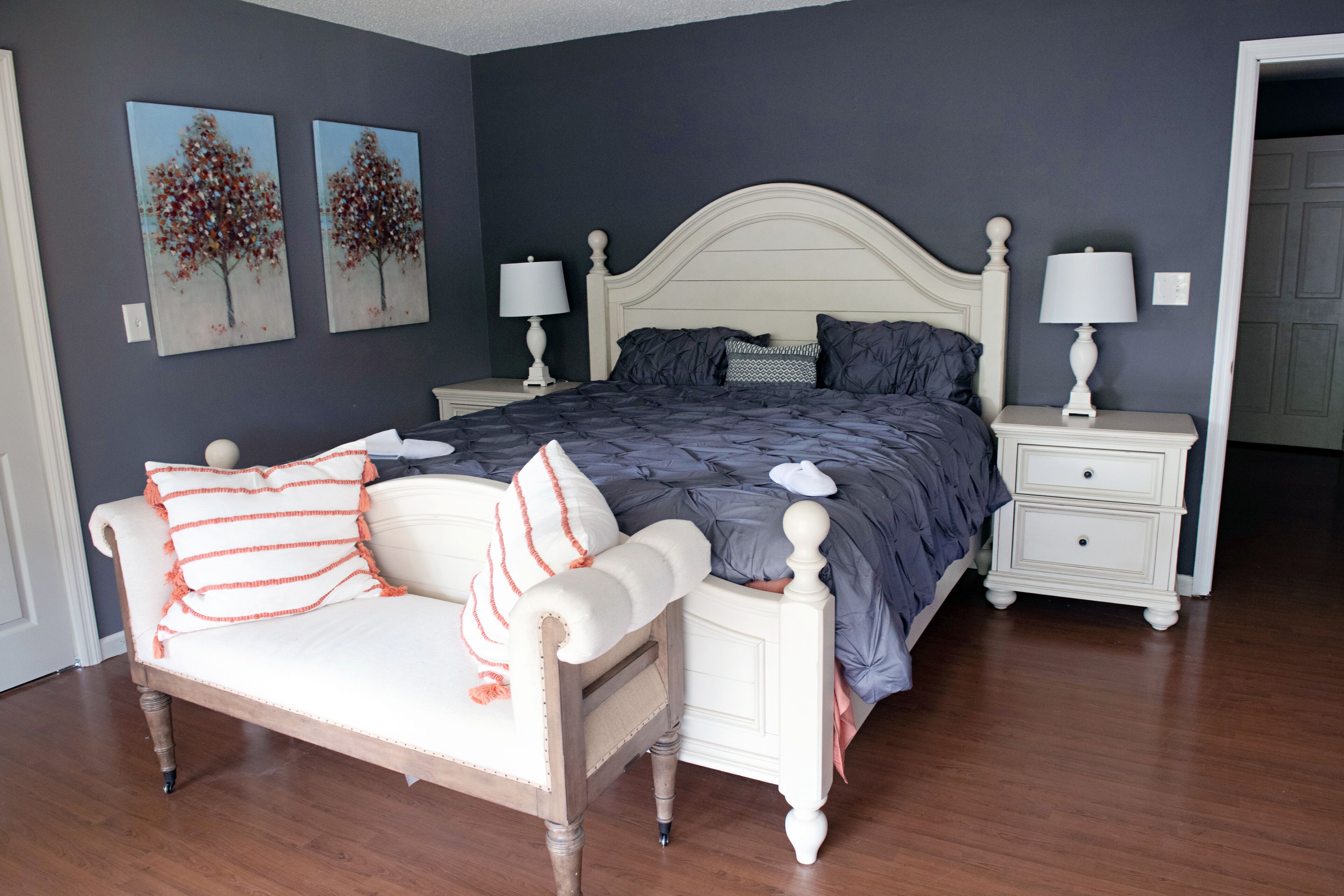 A bedroom with a bed, nightstands, a chair, and two paintings on the wall.