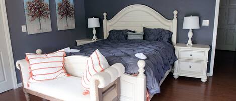A bedroom with a bed, nightstands, a chair, and two paintings on the wall.