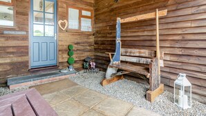 Une cabane en bois avec une porte bleue, un banc, une lanterne et un petit jardin.