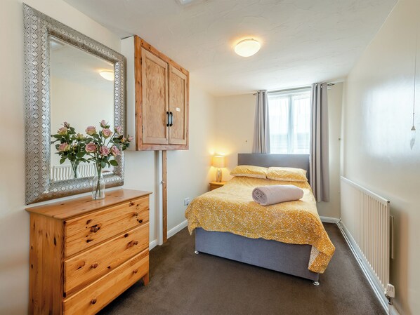 A bedroom with a bed, a dresser, a mirror, a window with curtains, and a radiator. - Captains Quarters - 16266 (Staithes, near Whitby)