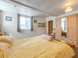 Un dormitorio con cama, armario de madera, una silla, un radiador y una ventana con cortinas.