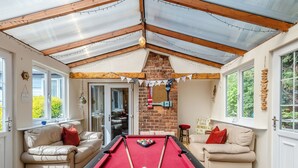 Une table de billard dans une pièce avec un plafond haut, des murs en briques et une vue sur la verdure à l’extérieur.