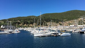 A marina with various boats docked, a building labeled 'CNS' in the background, and a hill with greenery. - House on the beach in Sesimbra (Sesimbra)