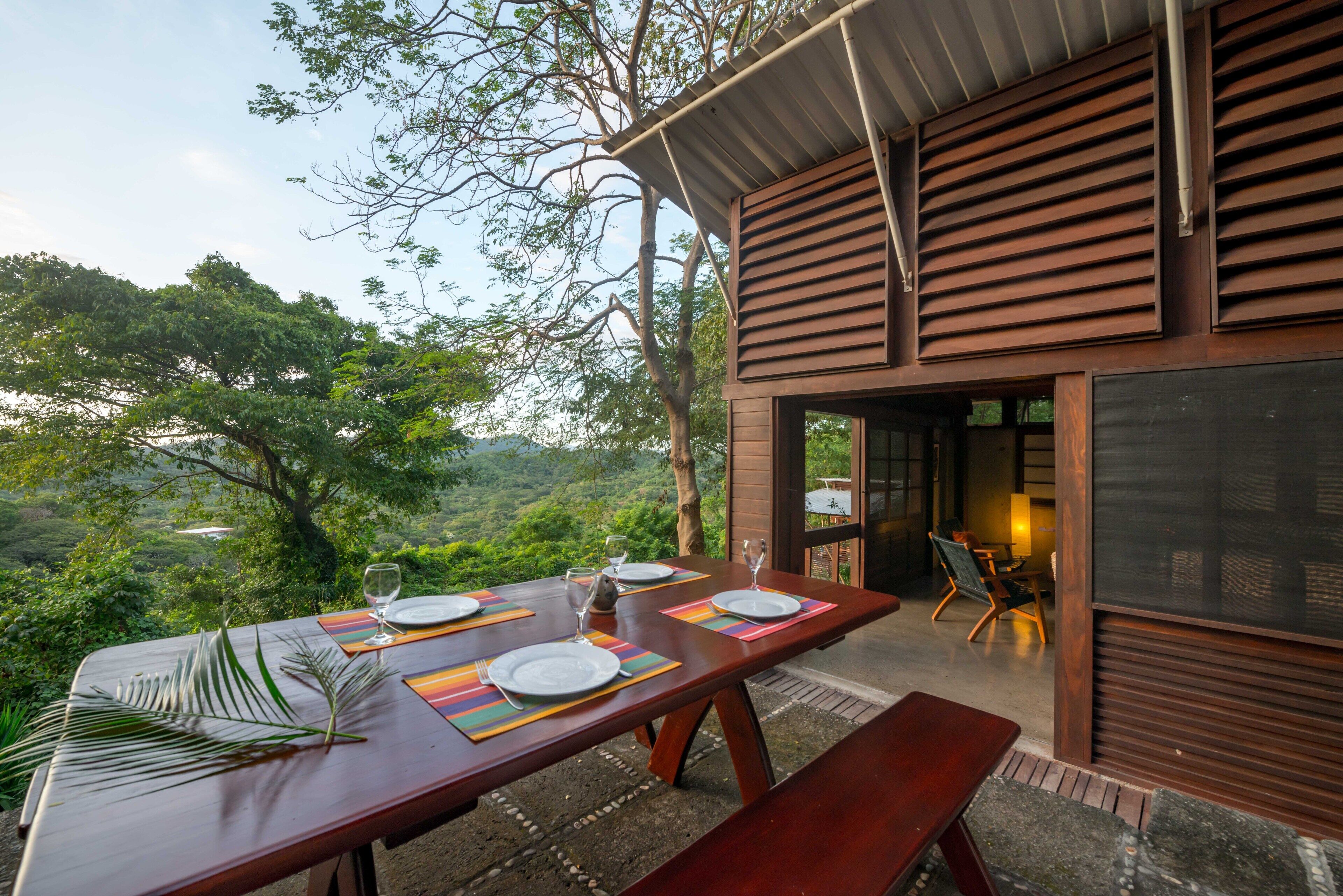 An outdoor dining area with a table set for four, overlooking a lush landscape.
