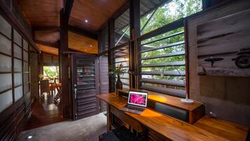 A modern interior with a wooden desk, laptop, and a view of greenery outside.