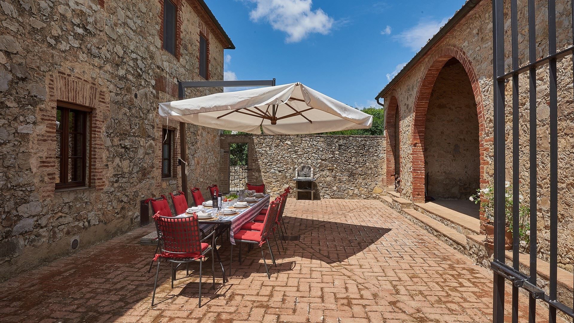 An outdoor dining area with a stone wall, a brick floor, and a table set for four with red chairs.
