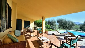 Uma área de estar coberta ao ar livre, com piscina, móveis de vime e vista para o campo.
