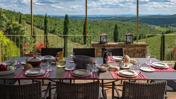 Un área de comedor al aire libre con una mesa preparada para cuatro personas, con vistas a un paisaje montañoso.