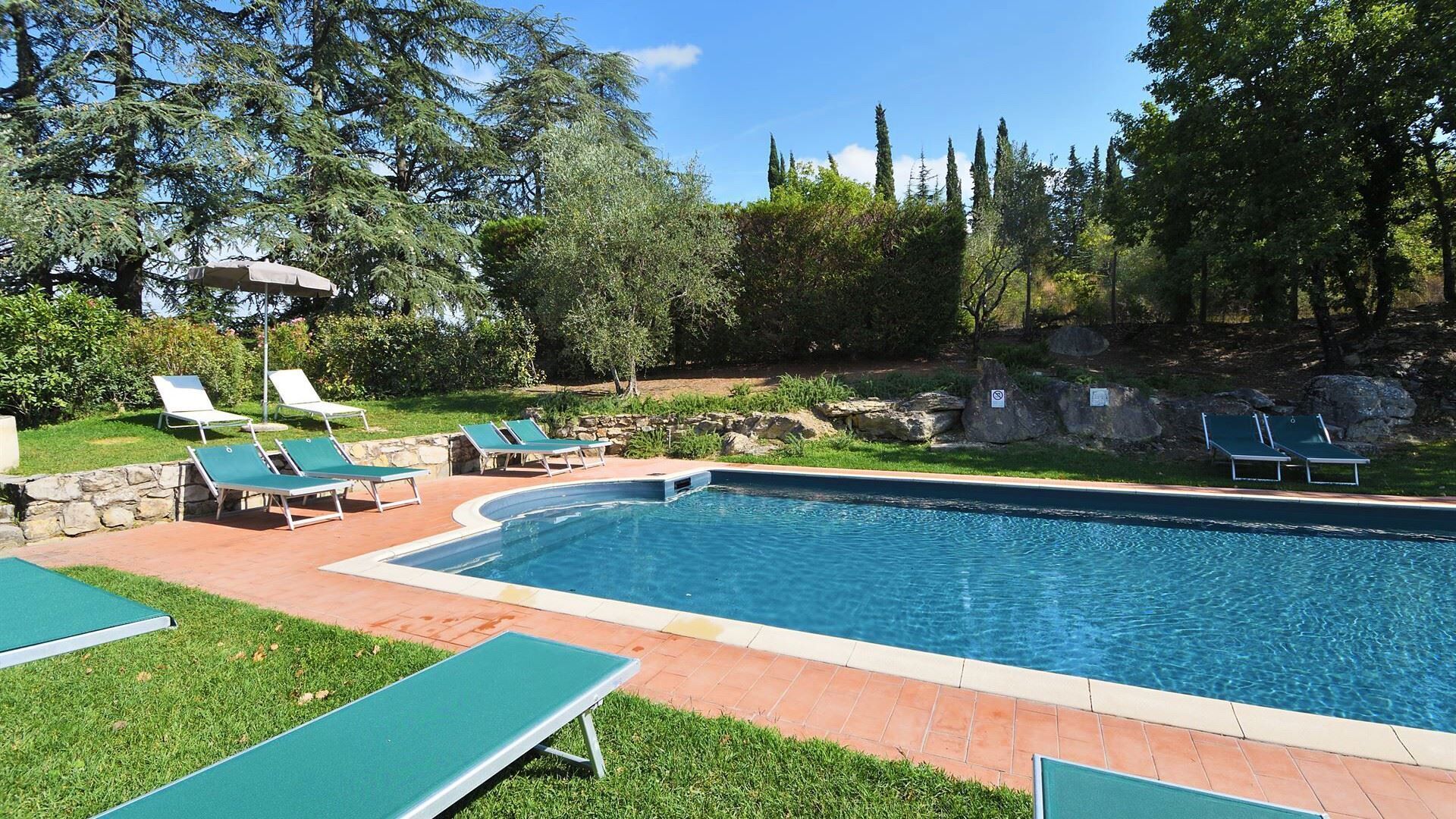 Una piscina rettangolare con bordo in pietra, circondata da un’area verde con diversi lettini.