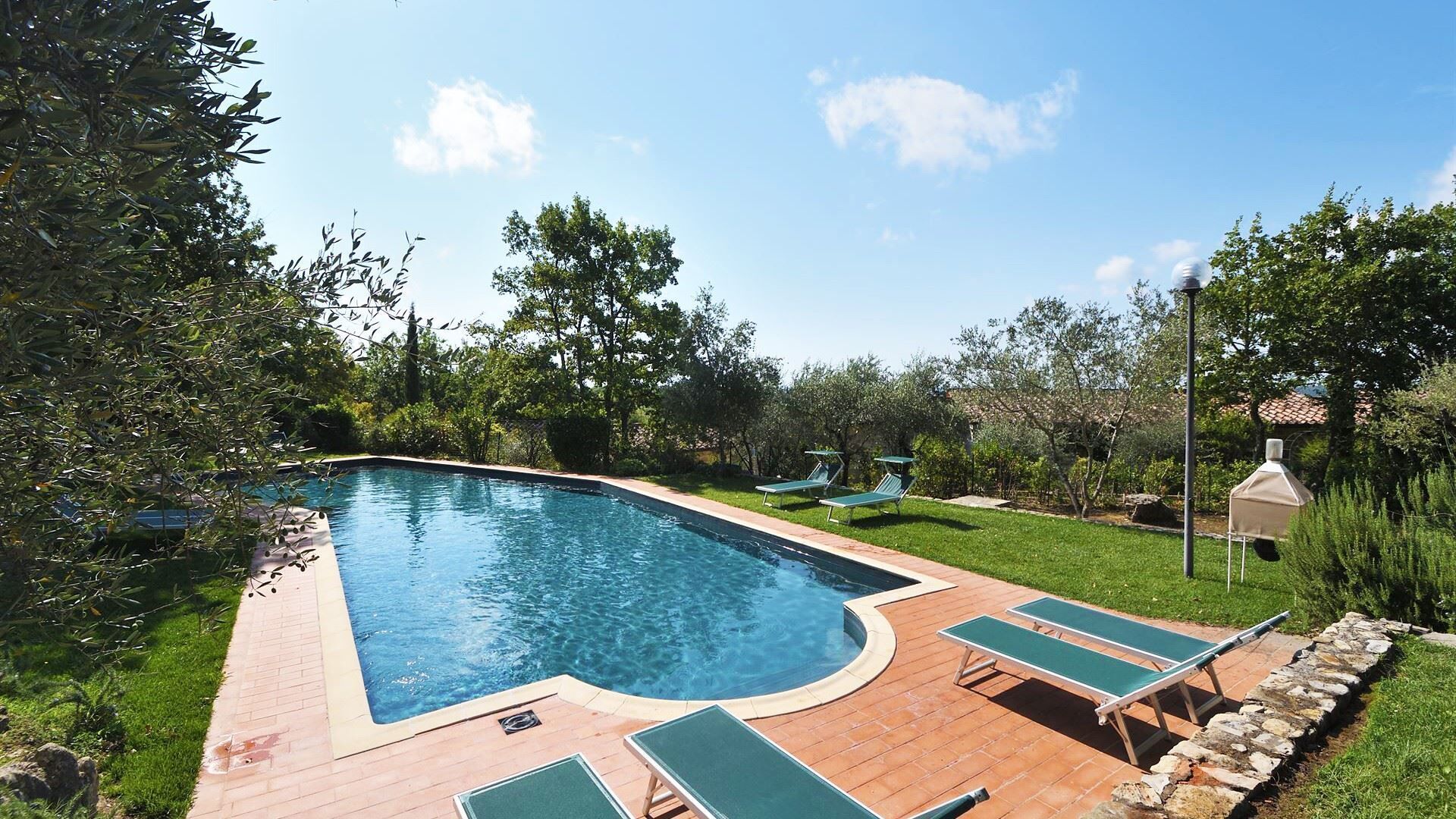 A swimming pool with a curved edge, surrounded by a brick deck and green lounge chairs.