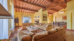 A spacious living room with a high wooden ceiling, a fireplace, and a dining area with a long table. - Macia Viva, Castellina in Chianti, Siena and Chianti (Castellina in Chianti)