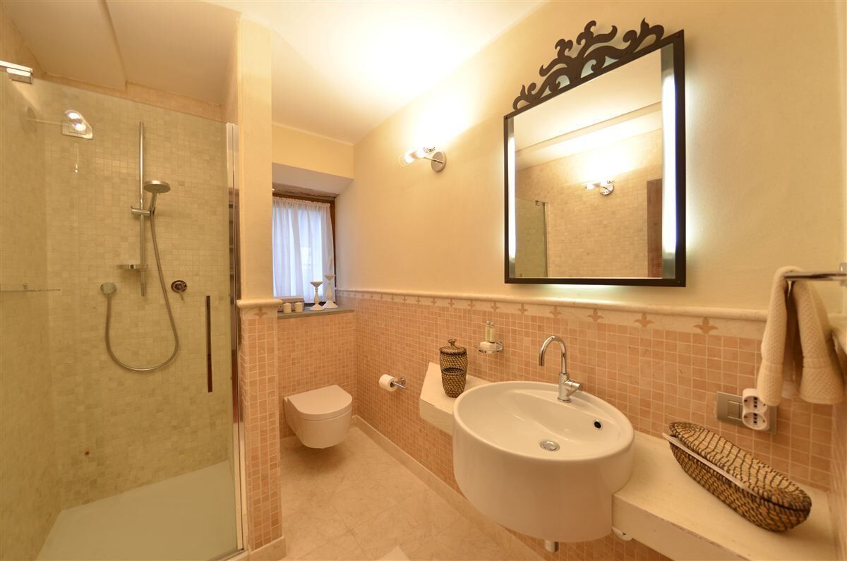 A bathroom with a glass-enclosed shower, a sink, a toilet, and a mirror.