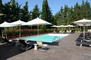 A poolside area with lounge chairs, umbrellas, and a clear blue pool.
