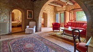 A room with stone walls, a red sofa, a white armchair, and a patterned rug.