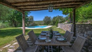 An outdoor dining area with a wooden table set for six, surrounded by stone walls and a pool in the background. - Villa San Michele, Gaiole in Chianti, Siena and Chianti (Gaiole in Chianti)