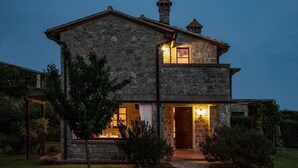 Una casa de piedra con estructura de dos pisos, una chimenea visible y una entrada iluminada.