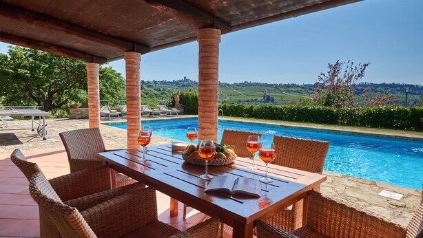 A poolside dining area with wicker furniture, a wooden table, and a view of a pool and landscape. - Casanovina, Castellina in Chianti, Siena and Chianti (Castellina in Chianti)