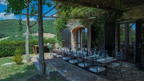 Un espacio de comedor al aire libre con una mesa y sillas de piedra, una pérgola y una pared de piedra con una ventana.