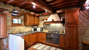 Une cuisine rustique avec des murs en pierre, des armoires en bois, une cuisinière à gaz, un four à micro-ondes et un évier.