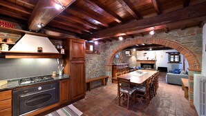Une cuisine rustique aux murs de pierre, aux poutres apparentes et dotée d’un coin repas agrémenté d’une cheminée en briques.