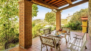 A covered patio with brick pillars, outdoor furniture, and a view of the countryside.