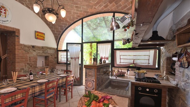 A rustic kitchen with a brick wall, a large window, a wooden table set for dining, and a basket of fresh vegetables. - Il Fornacino, Rapolano Terme, Siena and Chianti (Rapolano Terme)