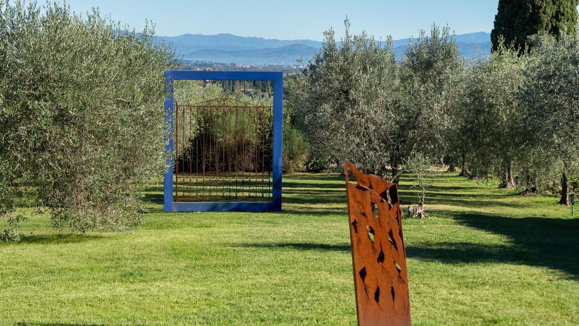 Une zone herbeuse avec une structure métallique bleue et une sculpture en bois.