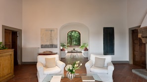 A spacious living room with two white armchairs, a coffee table, and a view through an arched window to a garden. - Castellare de Sernigi, Tavarnelle Val di Pesa, Florence and Chianti (Tavarnelle Val di Pesa)